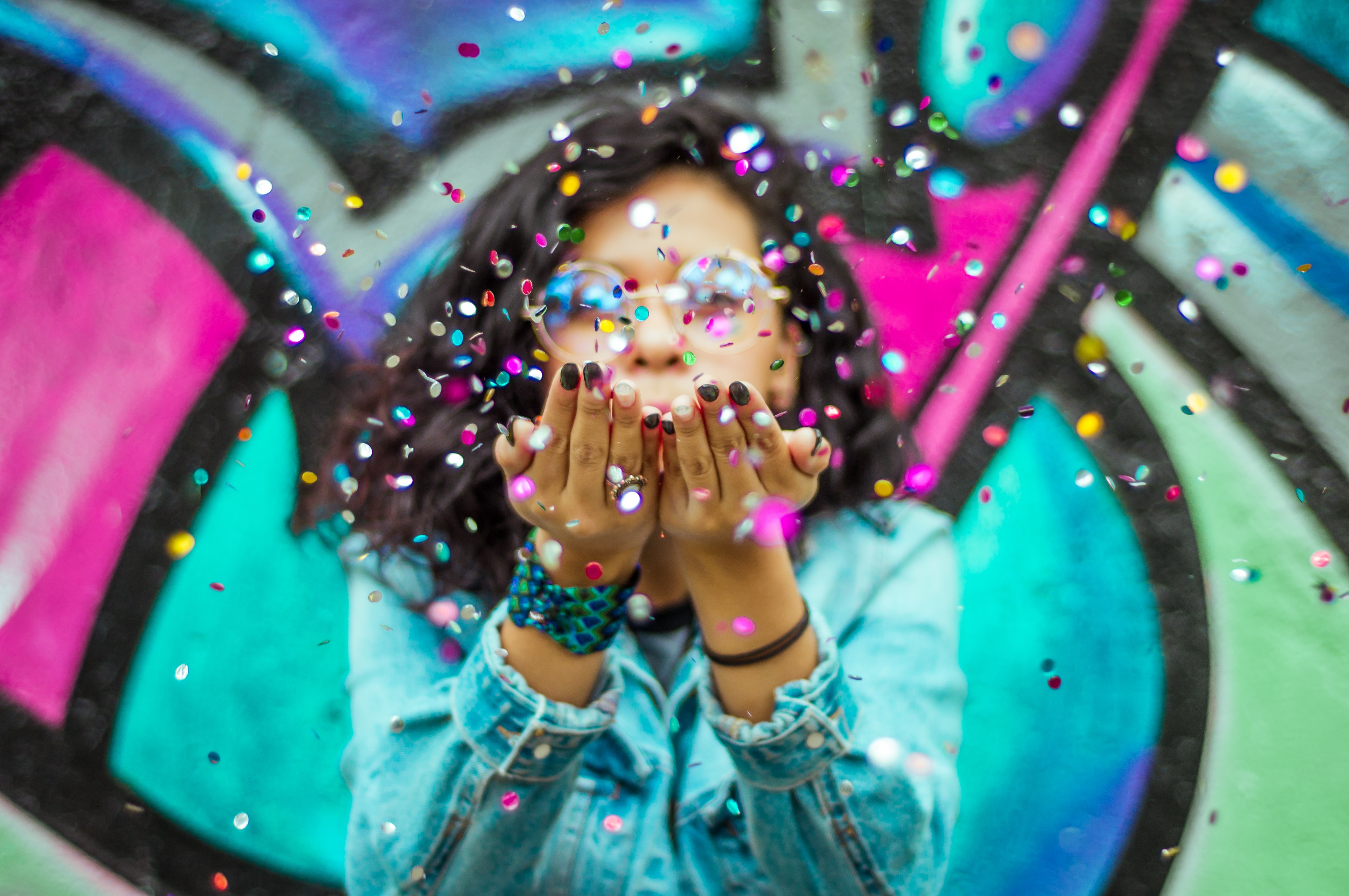 Persoon staat voor een graffitimuur en blaast confetti uit haar handen